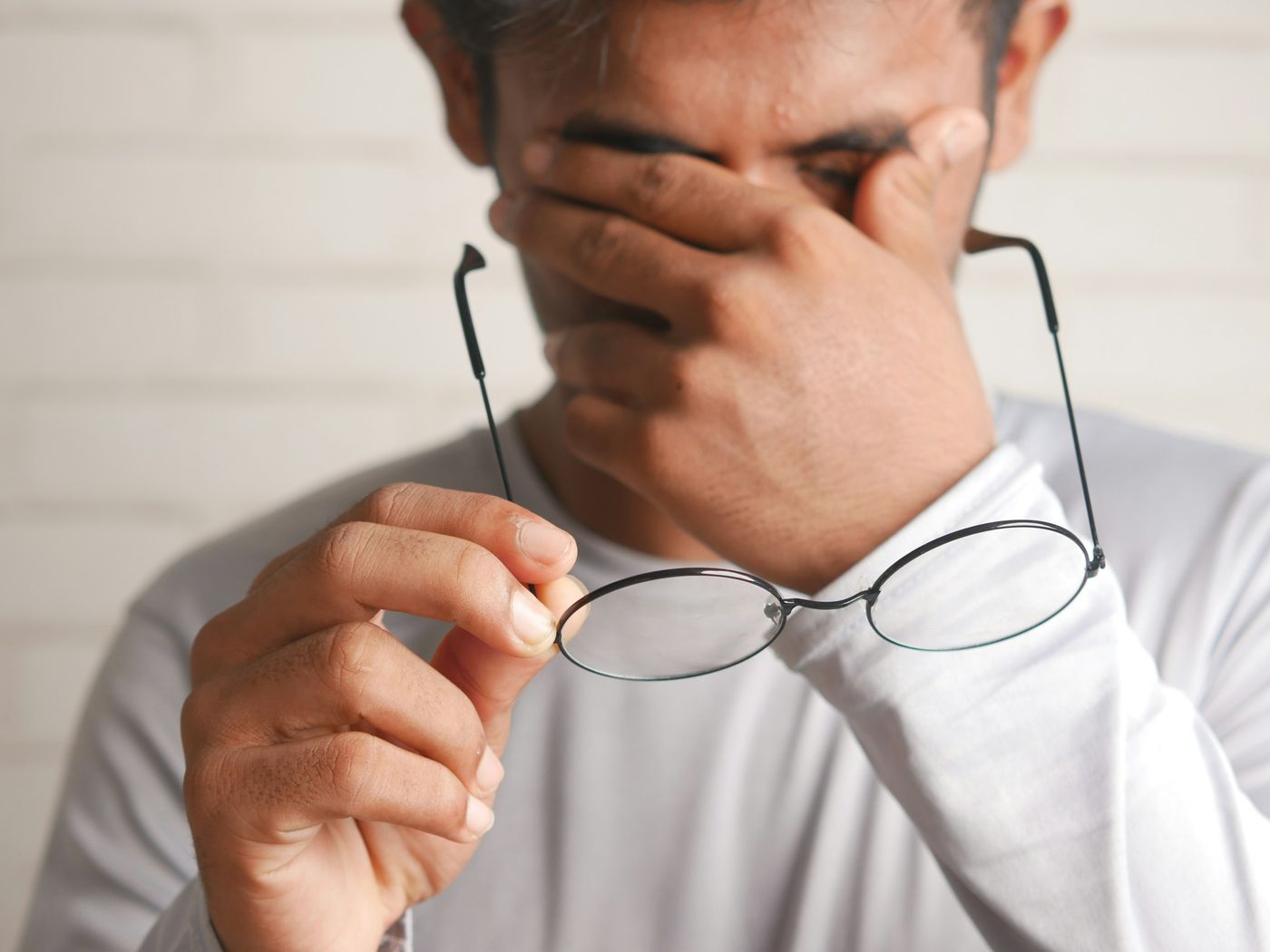 A man rubbing his tired eyes with one hand, holding his glasses in the other