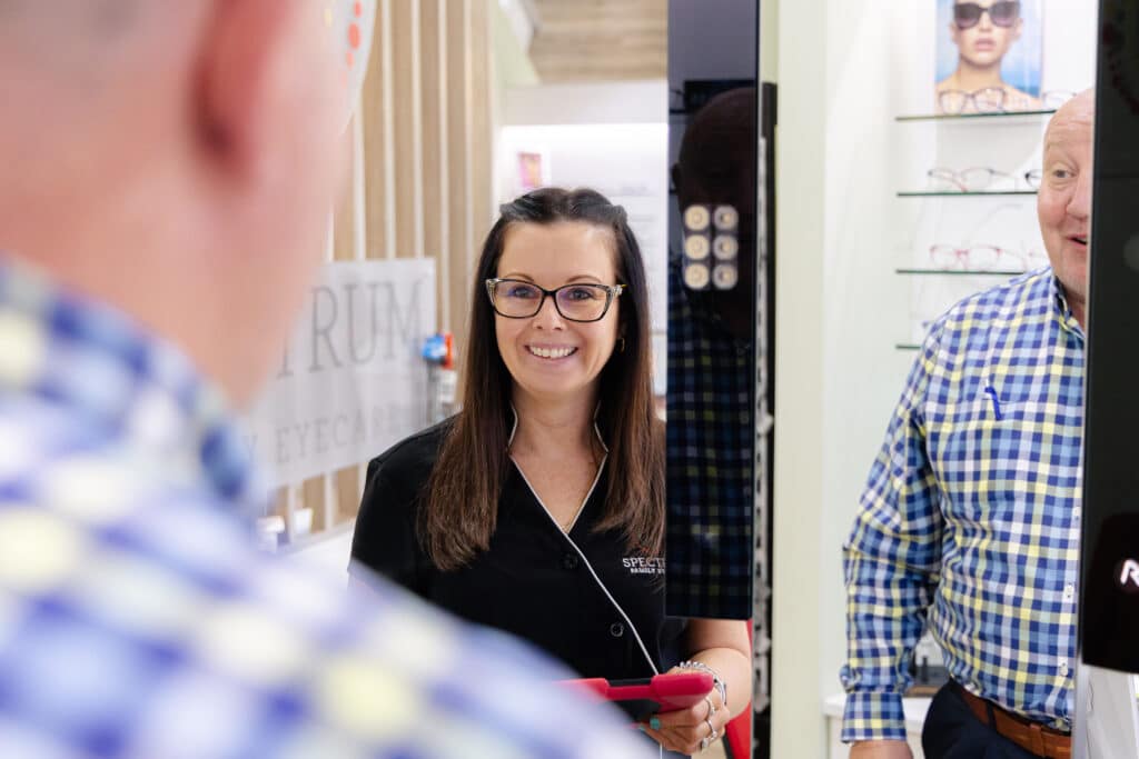Man in plaid shirt looking in a mirror with a smiling woman looking at the man